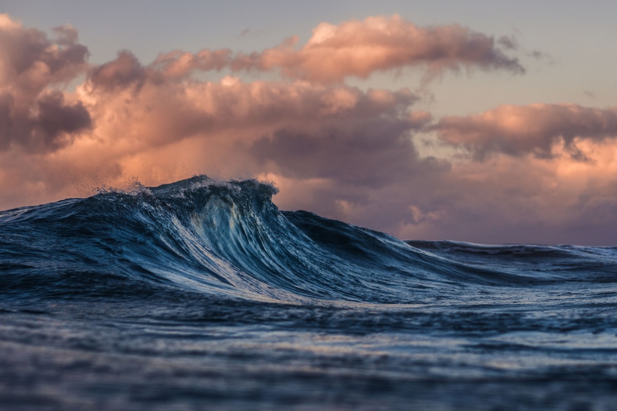 Ocean wave cresting at sunset under coral-colored clouds